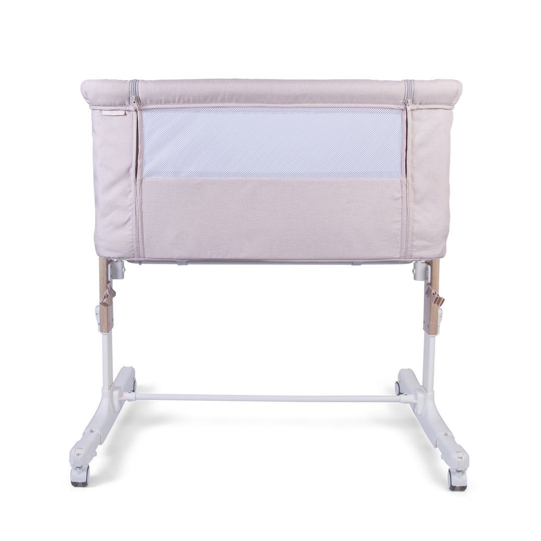 A beige Red Kite Rockabye Bedside Crib with mesh sides, adjustable height, and rocking base feature.